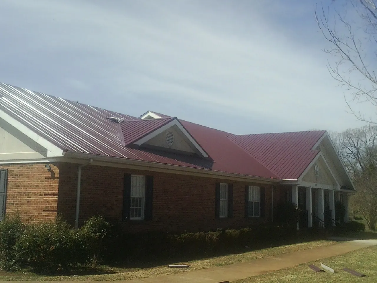 Red metal roof with gabled entries on a long brick building, from a Hail Damage Roof Repair job in Taylors