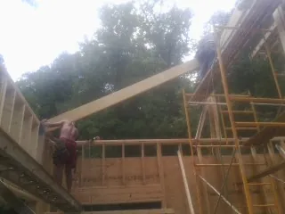 Carpenter raising a rafter beam on a new second story frame in Taylors