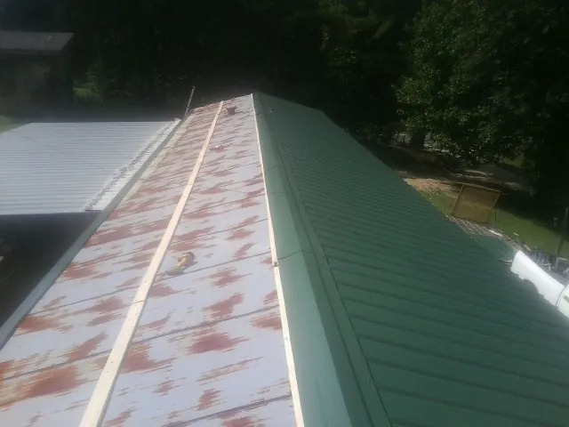 Old rusted panels beside newly installed green metal roofing — Wind Damage Roof Repair by Roofing Brothers in Taylors