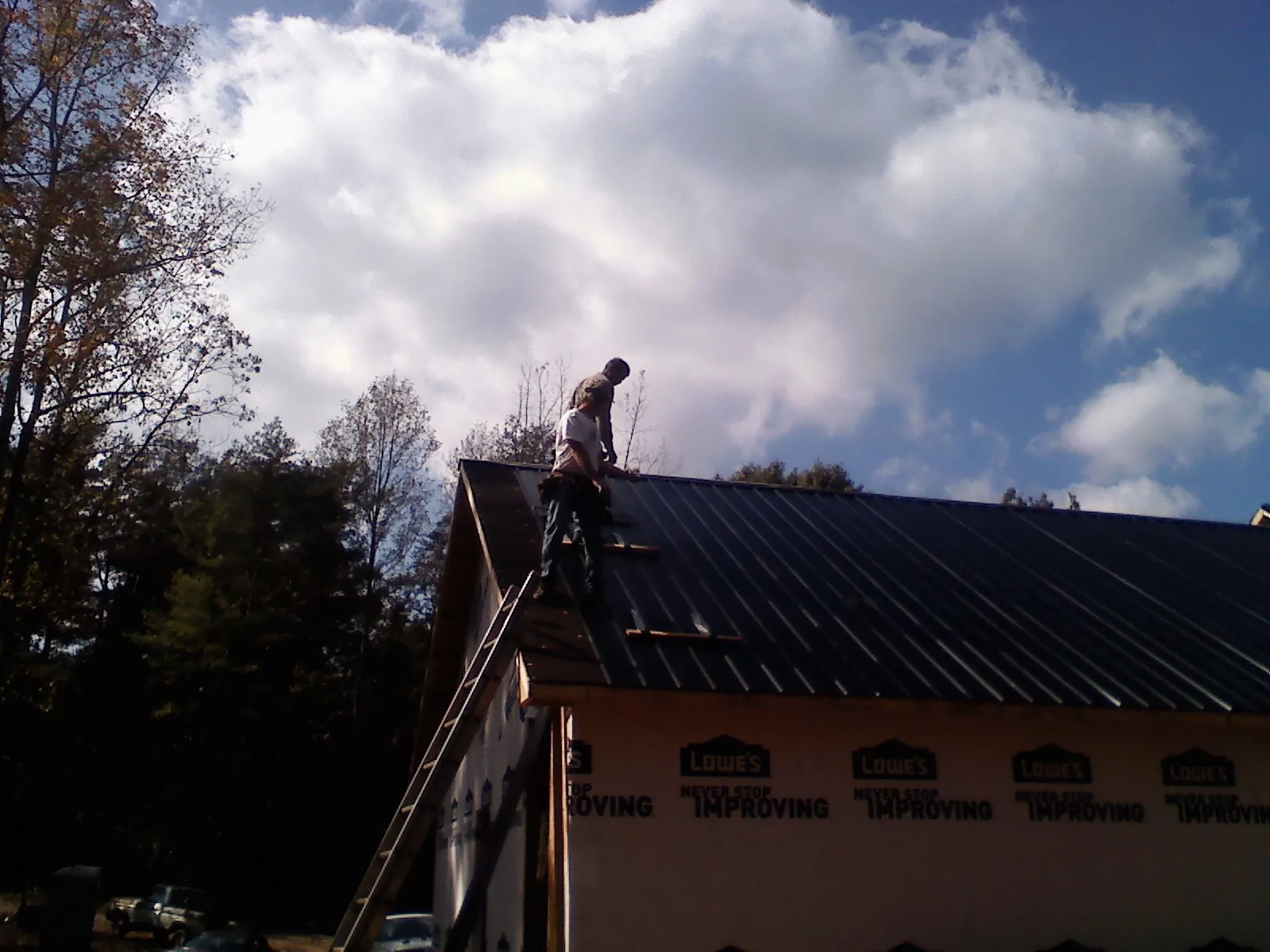 Roofer fastening dark metal panels high against a cloudy sky, from a Roof Inspection job in Taylors