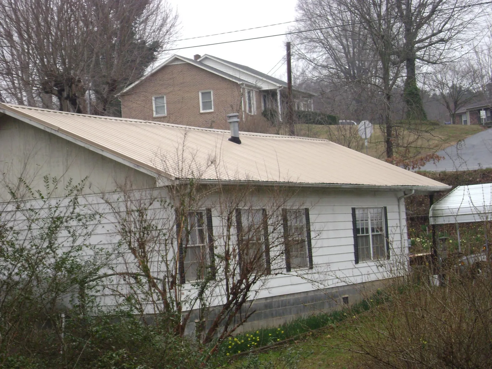Tan metal roof on a white sided house set into a hillside — Commercial Roofing by Roofing Brothers in Taylors